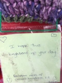 Post it note on a post box which reads "I hope this brightens up your day" - the post box has a knitted hat on it
