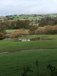 A view across the landscape with a stream, pool of water and farm buildings