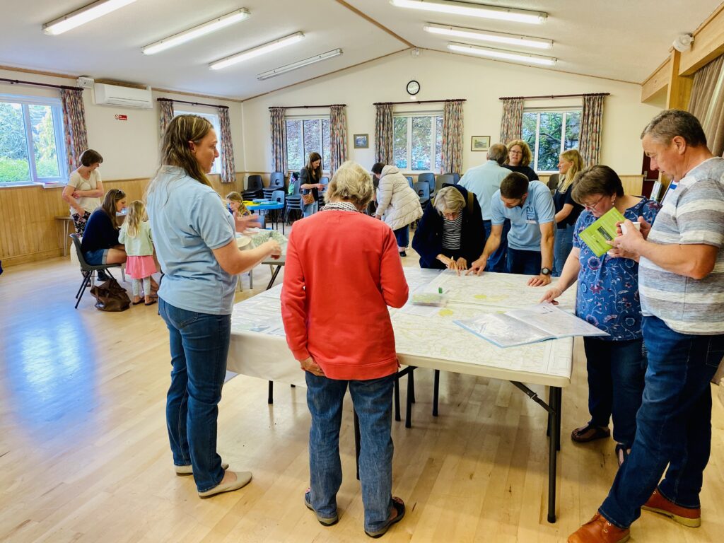 People in a village hall talking and looking at information on a table.